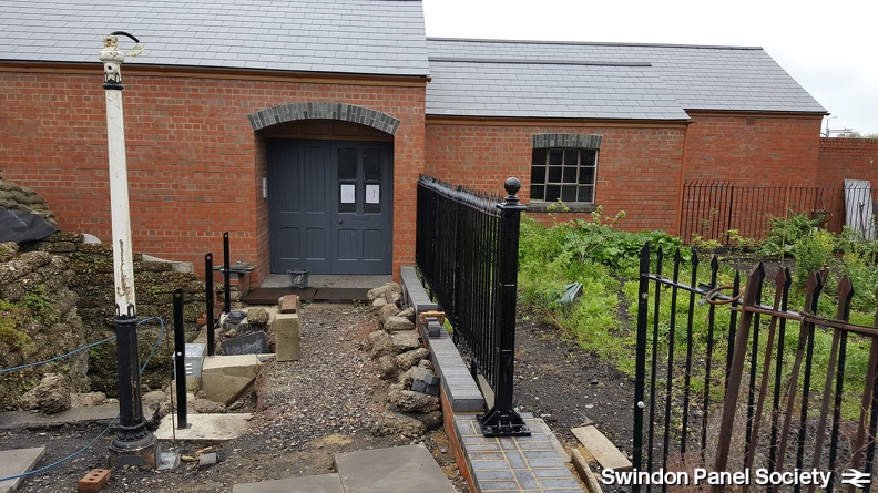 An updated building front entrance view, as fencing and railing posts continue to be worked upon.